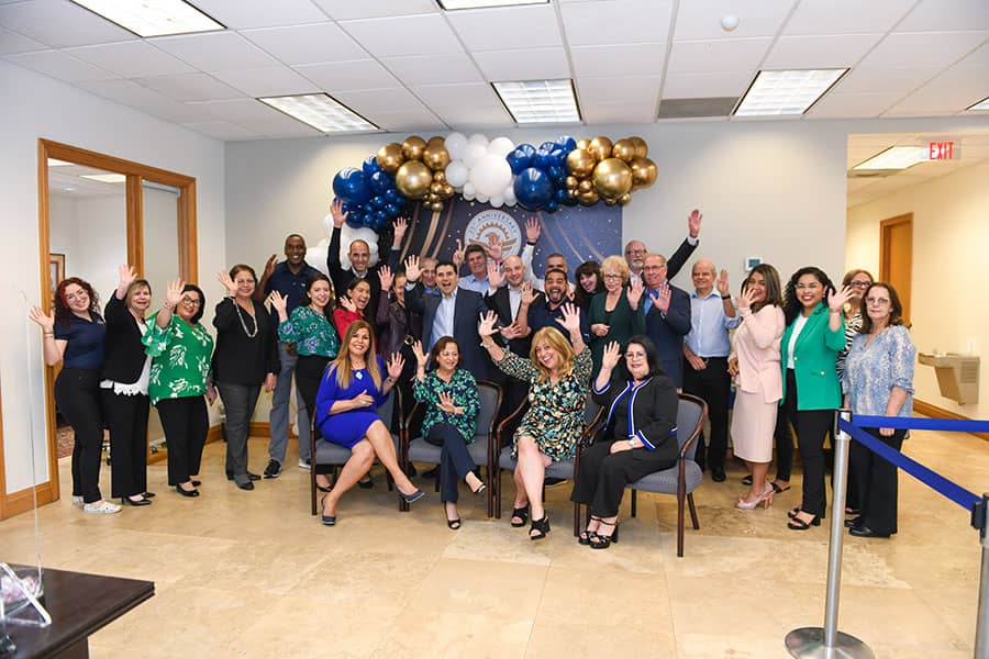 A group of Sunstate Bankers in the bank lobby  waving at the camera