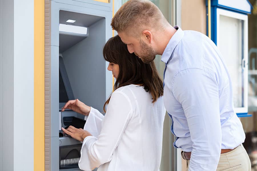 A man looking over a womans shoulder at an ATM