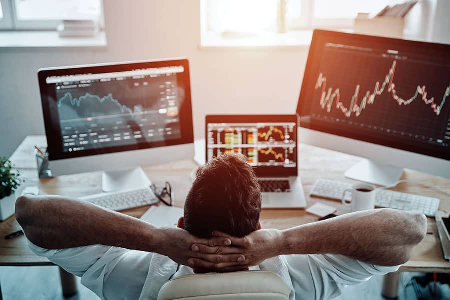 A man relaxing at his desk in front of 3 monitors