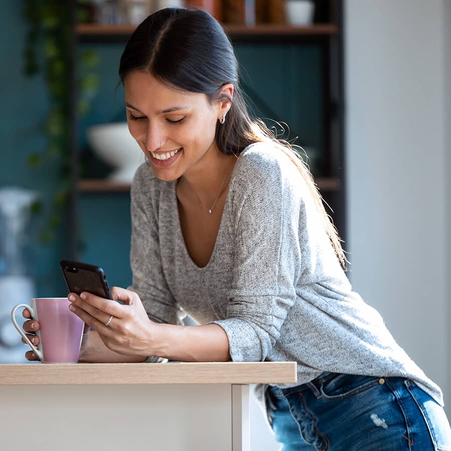 A woman having a cup of coffee and looking at her mobile phone screen