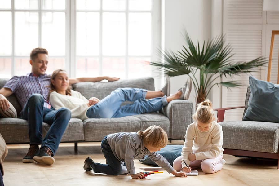 Parents on the couch watch their kids playing on the floor