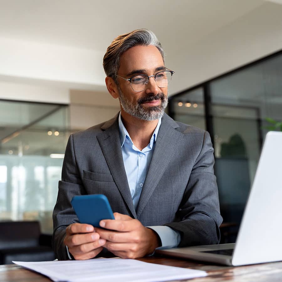A businessman holding a phone and looking at a laptop