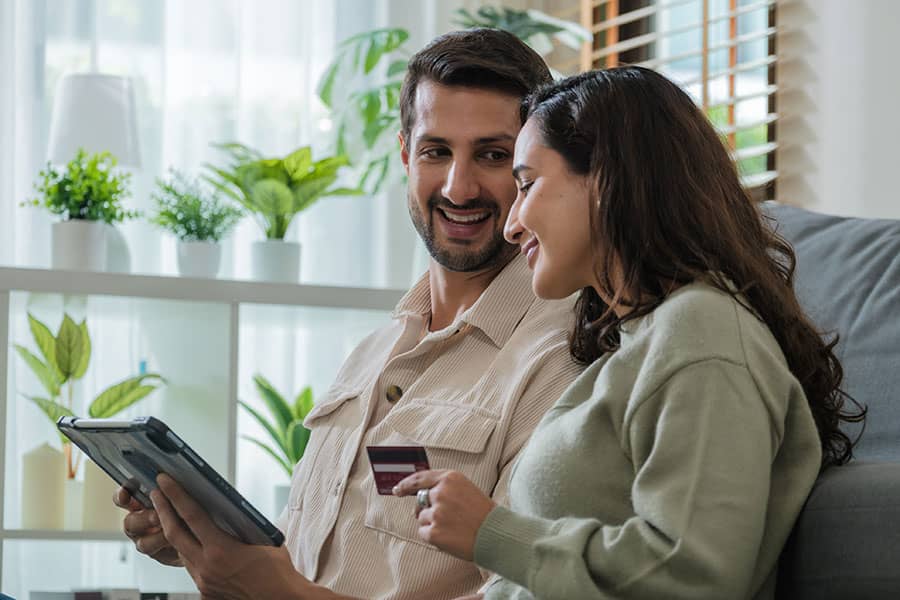 A couple sits on a couch and looks at their tablet